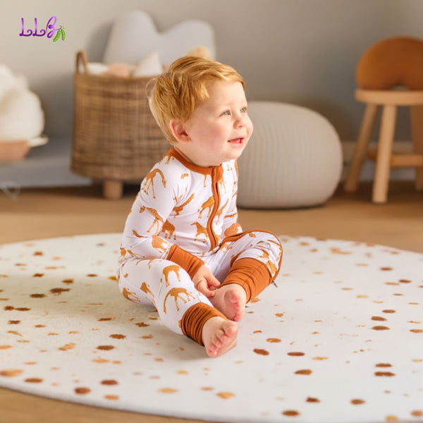 Happy toddler boy sitting in bedroom wearing a bamboo footless zip up romper with giraffe design.