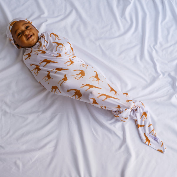 Happy baby, infant in a unisex giraffe print swaddle blanket and beanie set.  Made of bamboo viscose soft and stretchy large blanket that can be knotted or wrapped.  breathable, cute, good for sensative skin 