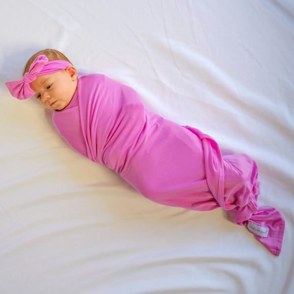 Pink soft baby girl swaddled in a bamboo viscose fabric swaddle blanket with a matching soft bow headwrap