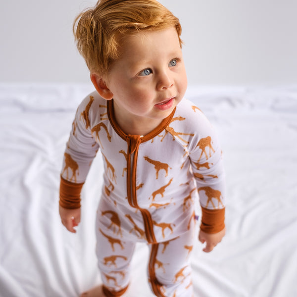 Boy toddler in footless convertible romper. Giraffe print with brown trim and double zipper. Bamboo viscose breathable fabric. Stretchy, soft, long lasting. 